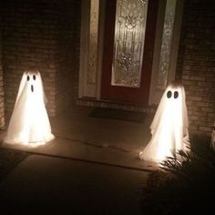 three white ghost statues in front of a door at night with lights shining on them