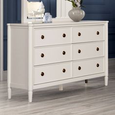 a white dresser with flowers on it in a blue and white room next to a mirror