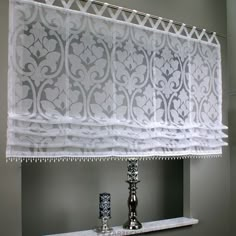 a white curtain hanging over a window next to a shelf with candles on top of it