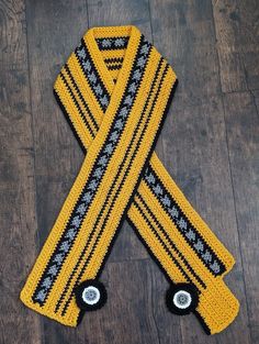 a crocheted yellow scarf with black and white stripes on it sitting on a wooden floor