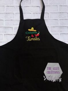 a black apron with the words cuisine and tamales on it next to a white brick wall