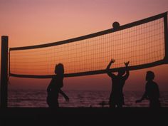 three people playing volleyball on the beach at sunset or dawn with net in foreground