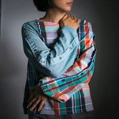 a woman with her arms crossed standing in front of a gray background wearing a plaid shirt