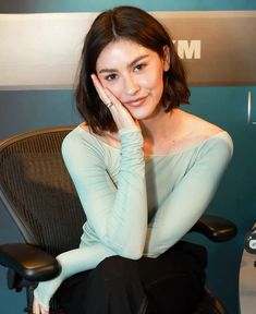 a woman sitting in a chair with her hand on her face and looking at the camera