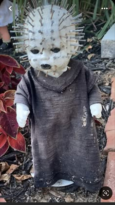 a creepy doll with spikes on its head is sitting in the ground next to some plants