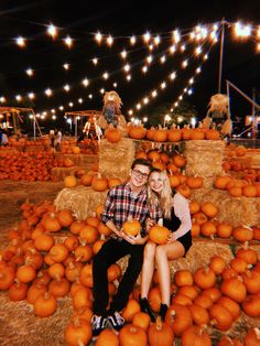 a man and woman sitting on hay bales with pumpkins in front of them