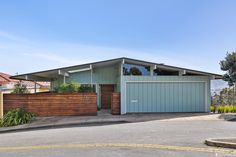 a blue house with a wooden fence around it's perimeter and trees in the background