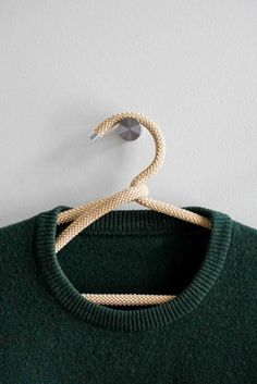 a green sweater hanging on a hanger with a white wall in the back ground