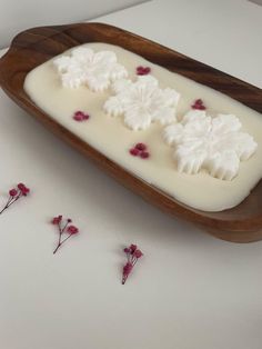 three small white flowers are placed on a wooden tray next to some tiny red and white flowers