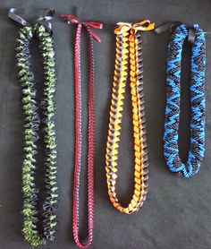 four different colored braided bracelets on a black surface with one tied up to the side