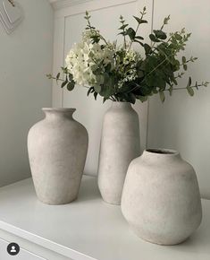 three vases with flowers in them sitting on a shelf