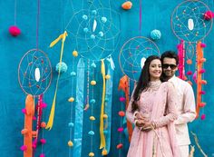 a man and woman standing next to each other in front of a wall with dream catchers