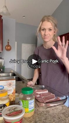 a woman standing in front of a kitchen counter with food on the counter and her hand up