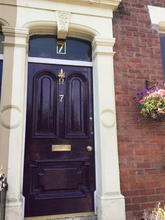 a purple front door on a brick building with flowers in the window boxes below it