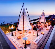 an outdoor area with white furniture and candles on the ground next to the ocean at dusk