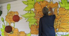 a woman is painting a mural on the side of a building with sunflowers