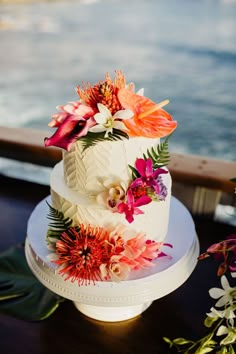 a three tiered white cake with flowers on the top and bottom is sitting on a table