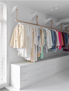 an organized closet with clothes hanging on the rack and white drawers in front of it