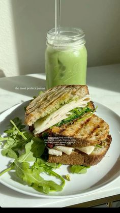 a sandwich on a white plate with a green smoothie