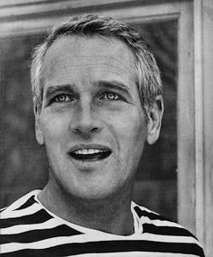 a black and white photo of a man in striped shirt looking at the camera with an intense smile on his face