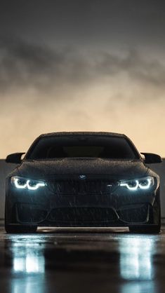 the front end of a black bmw car on a wet road with fog in the background