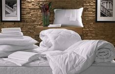 a bed with white sheets and pillows on it in a room that has brick walls