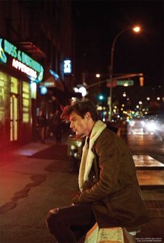 a man sitting on top of a wooden bench next to a street light at night