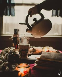 a person pours water into a teapot on a table with books and candles