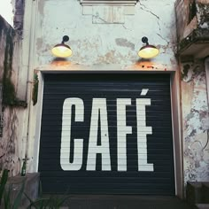 an old garage door with the word cafe painted on it and two lamps above it