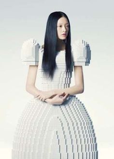 a woman with long black hair standing in front of a white background wearing a dress made out of legos