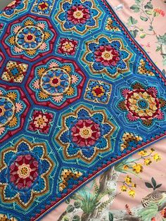 a blue crocheted blanket sitting on top of a bed covered in colorful flowers