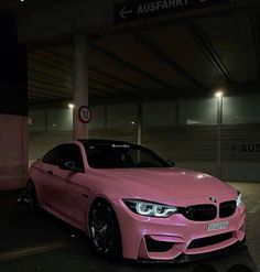 a pink car parked in front of a building at night with its hood up and lights on