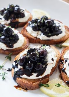 a white plate topped with bread covered in black olives and cream cheese next to lemon wedges