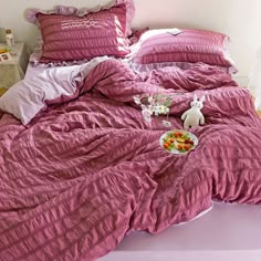 a bed covered in pink sheets and pillows with food on the bottom shelf next to it