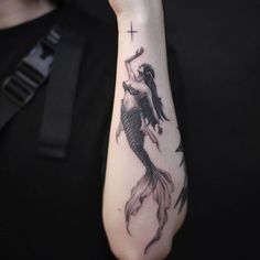 a woman with a cross on her arm and a mermaid tattoo on her left arm