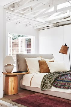 a bed with white sheets and pillows in a room next to a lamp on a table