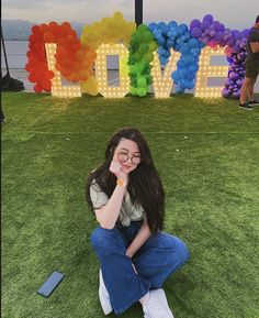 a woman sitting on the grass in front of a love sign