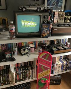 a television sitting on top of a book shelf next to a skateboard and movies