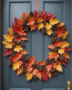 a wreath made out of pine cones and autumn leaves on a blue door with a red ribbon