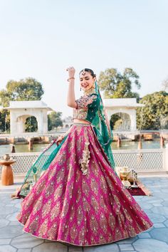 a woman in a pink and green lehenga dancing with her hands up to the sky