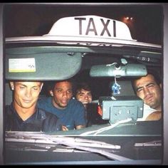 four men are sitting in the back of a taxi cab, looking at the camera