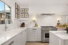 a white kitchen with marble counter tops and stainless steel appliances, along with pictures on the wall