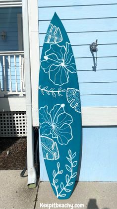 a blue surfboard with white flowers painted on it sitting in front of a house