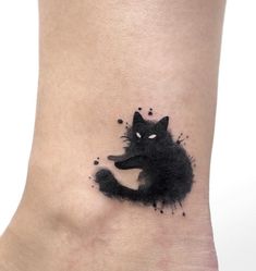 a black cat tattoo on the ankle with watercolor paint splatters all over it