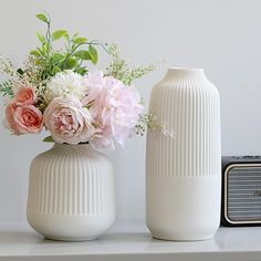 two white vases with pink and white flowers in them sitting on a shelf next to an old radio