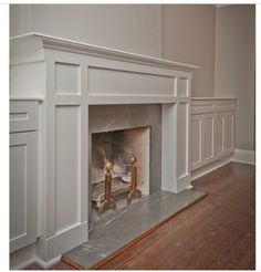 an empty living room with a fire place and white painted fireplace mantels on either side