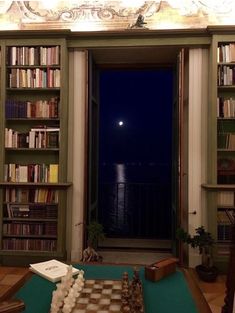 a chess board is sitting on a table in front of a bookcase and window