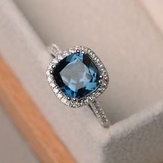 an engagement ring with a blue topaz surrounded by white diamonds in a gift box