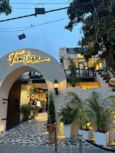 the entrance to tartar restaurant at dusk with palm trees and potted plants in front