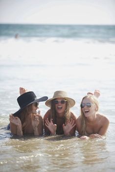 three women in the water with hats and sunglasses on, one is holding her hands up